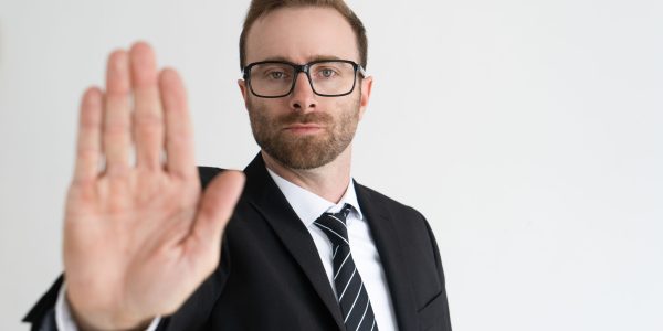 Serious business man showing open palm or stop gesture and looking at camera. Restriction concept. Isolated front view on white background.